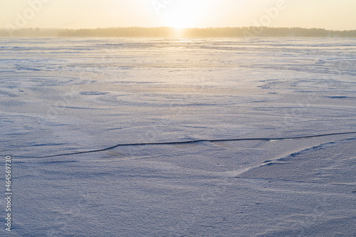 Sun shining above a frozen and snowy lake in Finland in the winter. Wintry  sunny and serene landscape at morning.