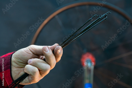 Professional bicycle workshop. The mechanic holds spokes in his hand on a black background. A fashionable and modern bicycle mechanic in a red plaid shirt on the background of a wheel.