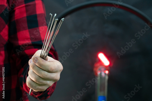 Professional bicycle workshop. The mechanic holds spokes in his hand on a black background. A fashionable and modern bicycle mechanic in a red plaid shirt on the background of a wheel.