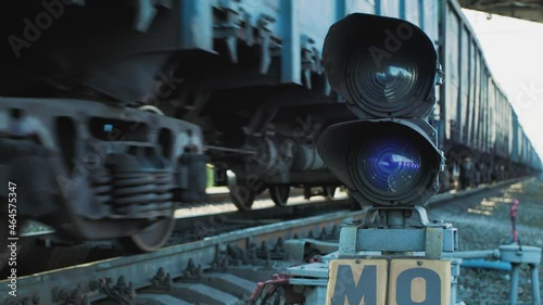 A long freight train is moving along the railway track in disfocus. The emphasis is on a semaphore system with a blue signal. Well-coordinated work of all services on the railway. photo