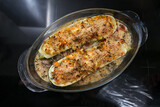 Oven baked zucchini stuffed with vegetables, feta cheese and parmesan in a glass casserole, healthy low carb diet meal, dark background with copy space, high angle view from above