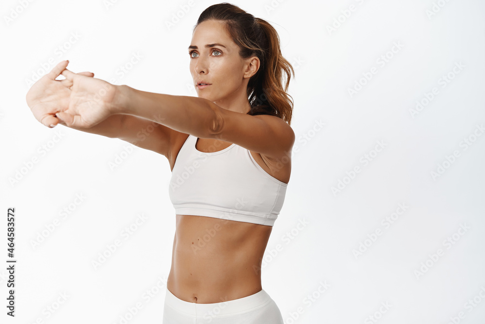 Fitness woman warm up, doing arms exercises in gym, stretching hands and looking focused, white background Fitness woman warm up, doing arms exercises in gym, stretching hands and looking focused, white background