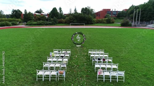 Wedding exit ceremony at the football running sports stadium. Wedding white decor arch chairs for guests on the grass. Wedding on the green field. A drone shot.