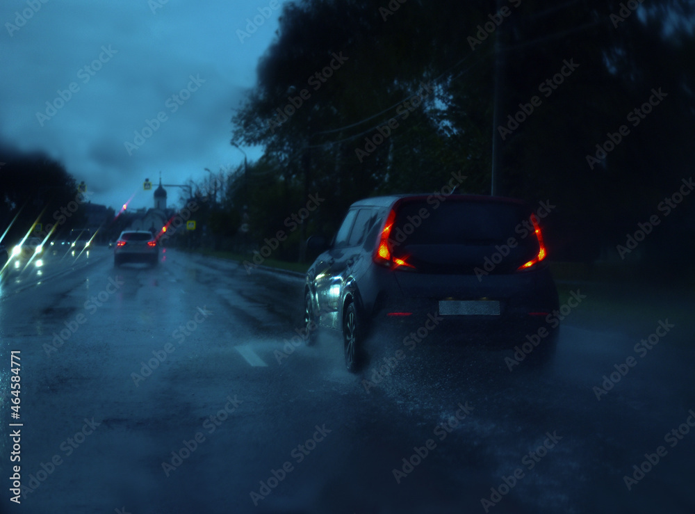 On a rainy autumn evening, cars race on wet asphalt, leaving a trail of splashes behind them.