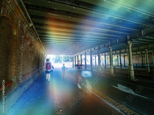 Light effect over Silhouettes of mother and child unrecognizable people on while fast motion under bridge with nearby sightseeing woman