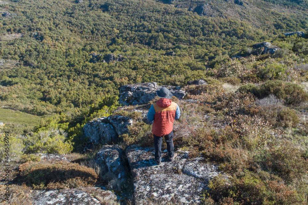 An adventurous man on top of a mountain looking at a mountain landscape in autumn.