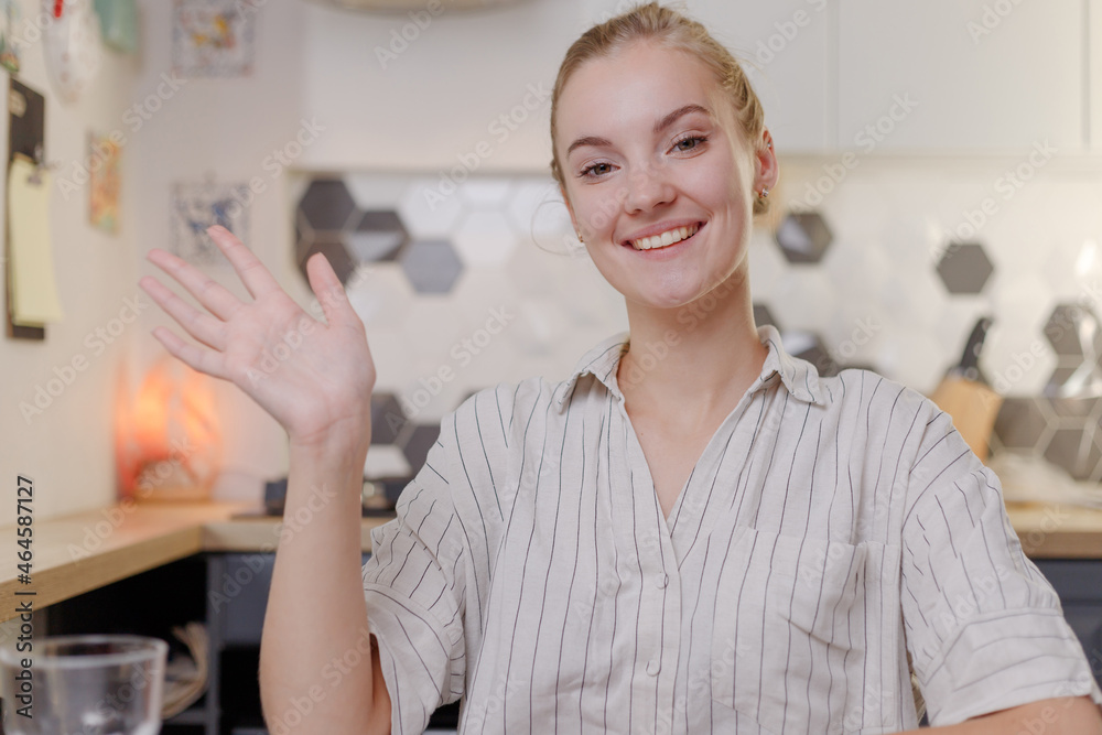 Smiling woman waving to camera chatting online at home