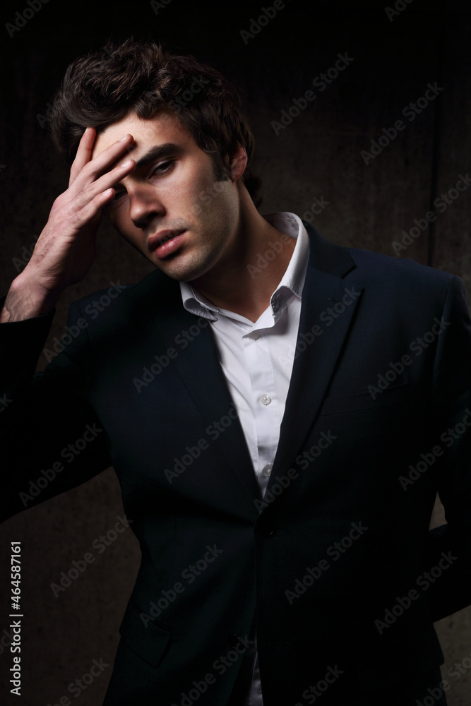 Fototapeta premium Thinking charismatic man posing and looking serious on dark shadow dramatic light background. Closeup portrait. Art light and shadow.
