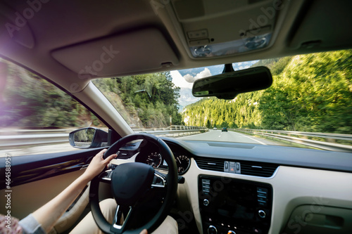 Woman driving luxury car on the difficult road highway in French mountains near MOnt-Blanc with large luxury car interior and defocused perspective over mountains © ifeelstock