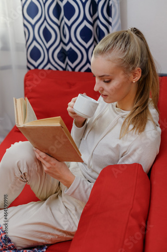 Woman on coah with old book and cup of coffee in hands photo