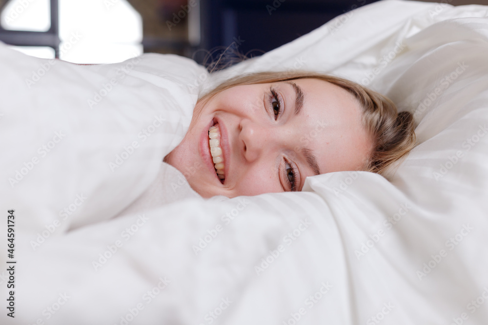 Portrait of young woman lying in bed with white linens Portrait of young woman lying in bed with white linens