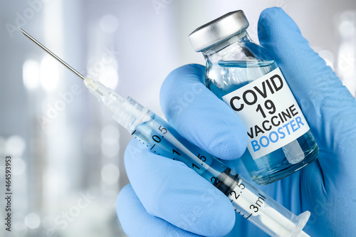 Schilderij op canvas Hand in blue medical gloves holding a syringe and vaccine vial with Covid 19 Vaccine Booster text, for Coronavirus booster shot