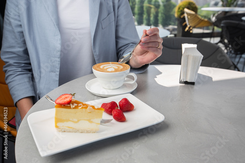 Girl enjoy classic cheesecake with fresh strawberry with cup of coffee on white table. Close Up view. Tasty breakfast. Piece of cake on plate, white cup on white marble background.