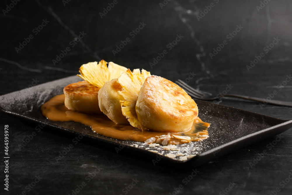 Cottage cheese pancakes, Syrniki or Cheesecakes with dried pineapple and caramel isolated on black marble background. Homemade food. Tasty breakfast. Selective focus.