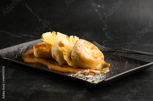 Obraz na płótnie Cottage cheese pancakes, Syrniki or Cheesecakes with dried pineapple and caramel isolated on black marble background. Homemade food. Tasty breakfast. Selective focus. w salonie