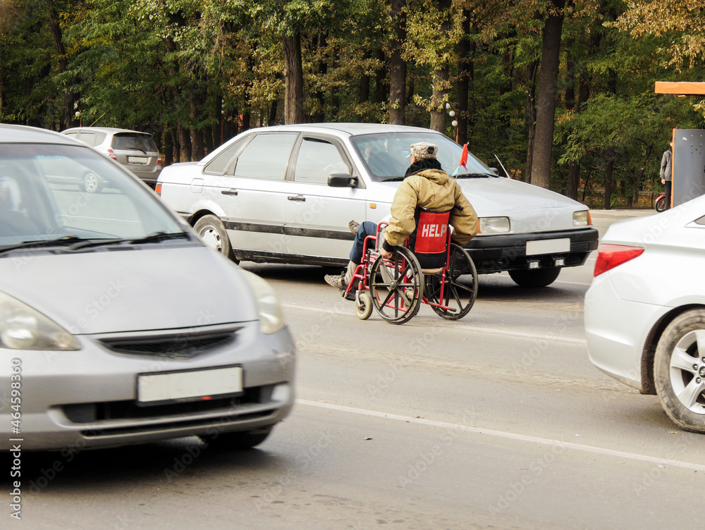 A disabled person in a wheelchair begs on the highway. The inscription on the wheelchair A disabled person in a wheelchair begs on the highway. The inscription on the wheelchair