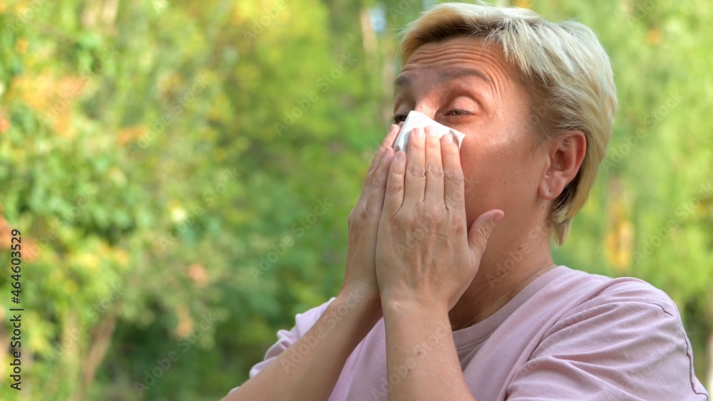 A girl with blonde hair and a short haircut sneezes from allergies and wipes her nose with a napkin A girl with blonde hair and a short haircut sneezes from allergies and wipes her nose with a napkin