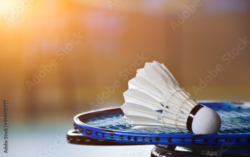Cream white badminton shuttlecock and racket with neon light shading on green floor in indoor badminton court, blurred badminton background, copy space. photo