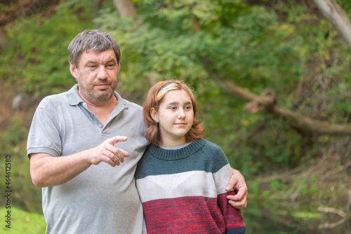 a teenage girl with a short haircut in a warm sweater with her dad in nature against the background of green nature in early autumn © Petr