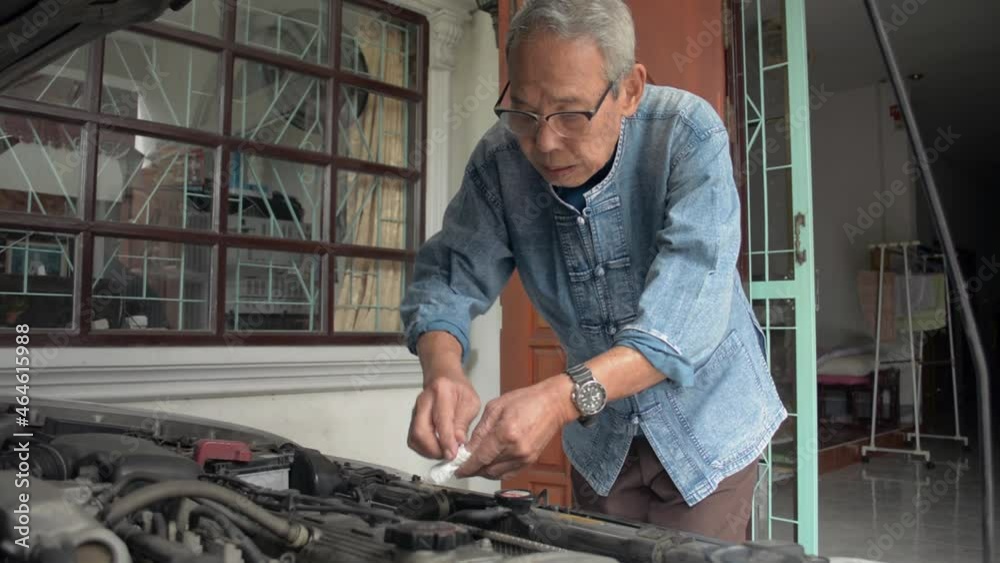 Asian senior retired man in eyeglasses cleaning and checking engine parts of his old car after fixing at home. Vehicle maintenance. Retirement life.