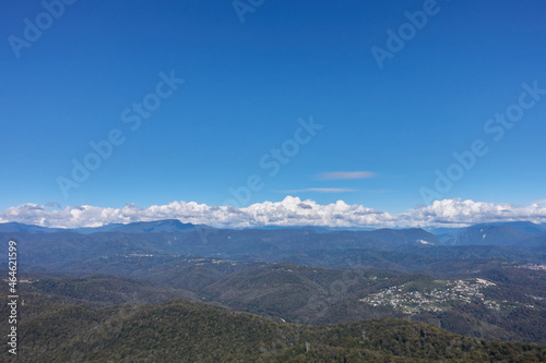 Bird's eye view of a mountain village, white cumulus clouds, forest and mountains.