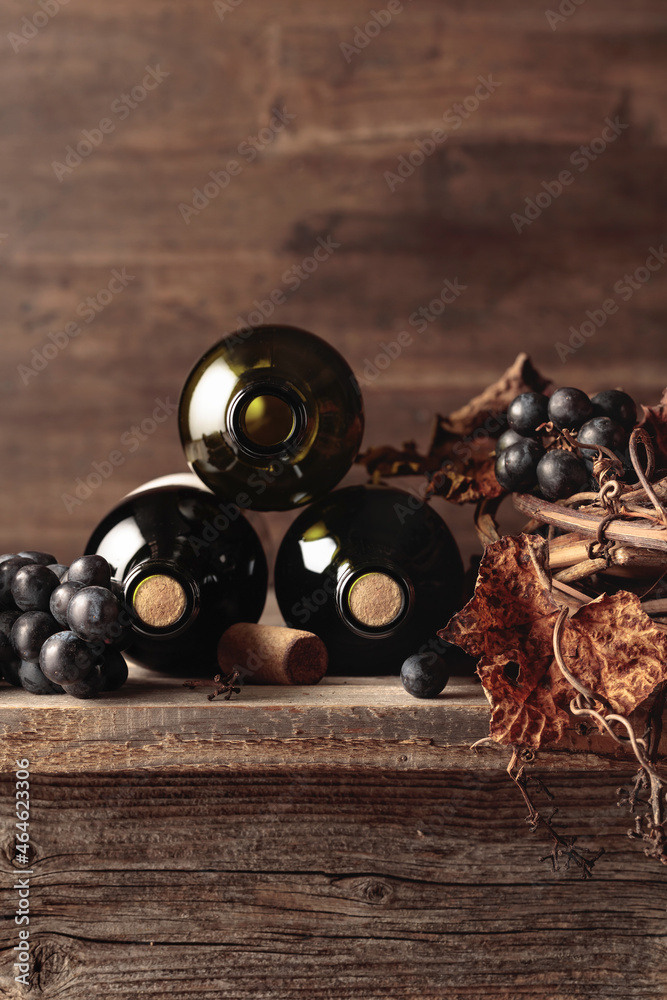 Bottles of red wine with grapes and dried vine on an old wooden table ...