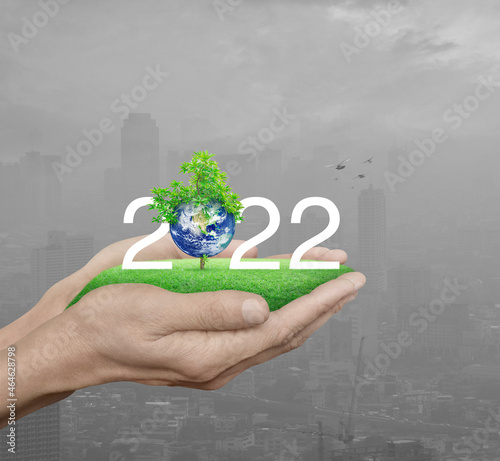 2022 white text with planet and tree on green grass field in man hands over pollution city tower and skyscraper with birds, Happy new year 2022 ecological cover, Save the earth concept, Elements of th
