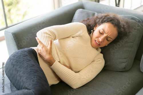 Latin woman lying down on sofa with stomachache feeling photo