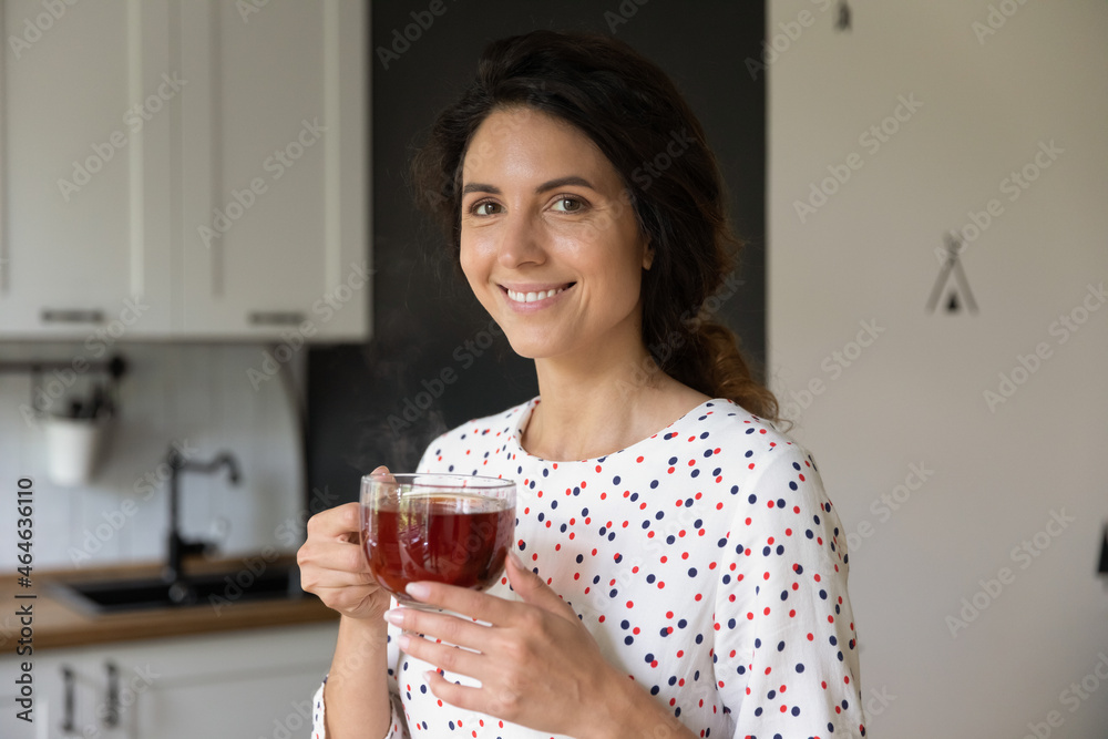 Happy Hispanic woman drinking yellow tea at home, holding big glass mug, looking at camera and smiling. Female homeowner taking break, enjoying hot morning aromatic beverage in kitchen Happy Hispanic woman drinking yellow tea at home, holding big glass mug, looking at camera and smiling. Female homeowner taking break, enjoying hot morning aromatic beverage in kitchen