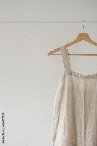 Minimalist wardrobe: Neutral beige colour overall dress or sundress on hanger against white wall. Aesthetic fashion concept