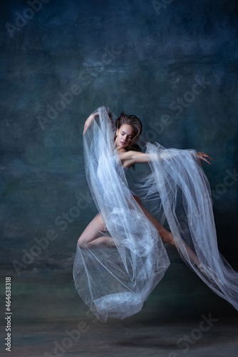 Studio shot of young flexible ballerina dancing isolated on dark vintage studio background. Art, motion, action concept.