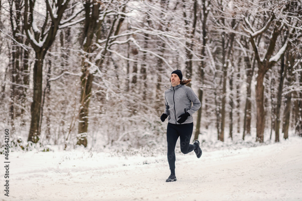 Fast runner running in woods at snowy winter day. Healthy habits, outdoor fitness, chilly weather