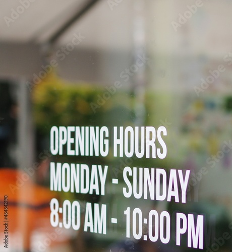 Opening hour sign white decal sticker on store window glass. Monday to Sunday. 8 am to 10 pm. photo
