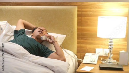 Sleepy Asian man is picking up the phone on his comfortable bed. Boring freelancer lifestyle concept.