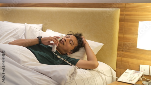 Sleepy Asian man is picking up the phone on his comfortable bed. Boring freelancer lifestyle concept.