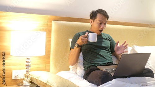 Surprised Asian man working with his laptop on his bed. Freelance problem concept.