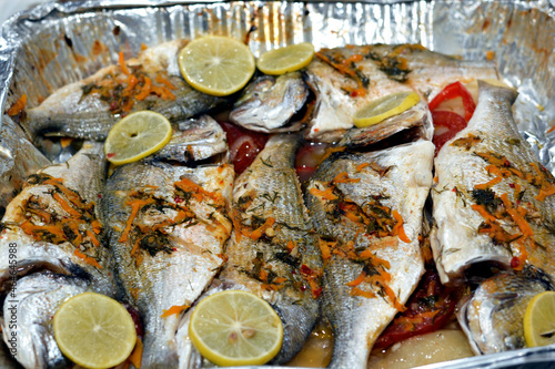 Seafood cuisine, sea bream fishes cooked in the oven with lime slices, tomatoes and onion rings in a foil plate, gilt-head bream fishes recipe, denise fish cooked, selective focus photo