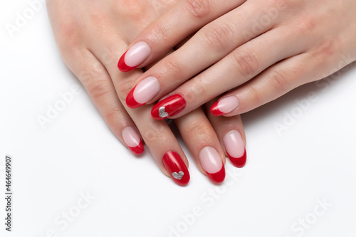 Nail design for Valentine's day. Red French manicure with painted silver hearts on the ring fingers in a close-up of long oval nails on a white background.