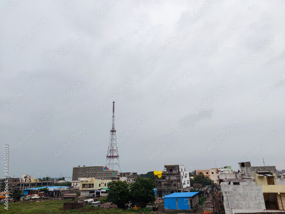 Stock photo of top view of cityscape. Tall mobile network tower installed outskirts of the developing city surrounded by houses and commercial buildings. Dark clouds covered the sky in evening time .