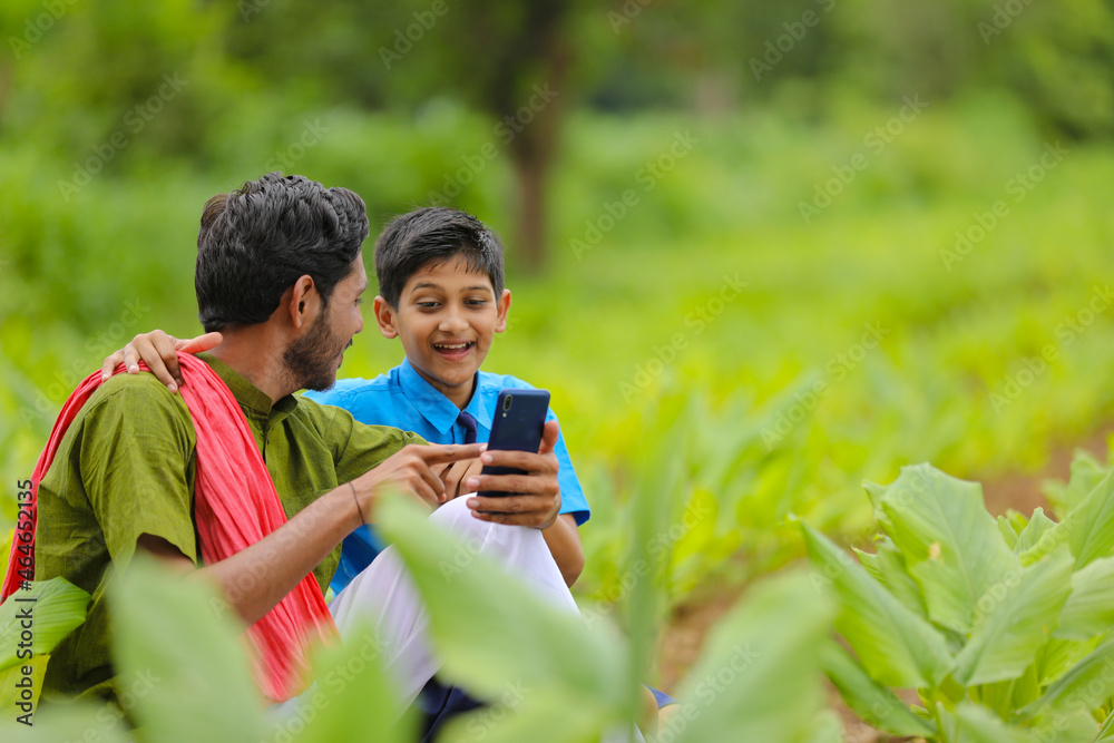 Fototapeta premium Indian farmer using smartphone with his child at green turmeric agriculture field.