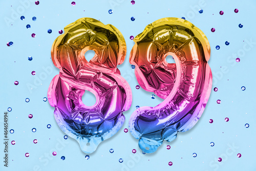 Rainbow foil balloon number, digit eighty nine on a blue background with sequins. Birthday greeting card with inscription 89. Top view. Numerical digit. Celebration event, template. photo