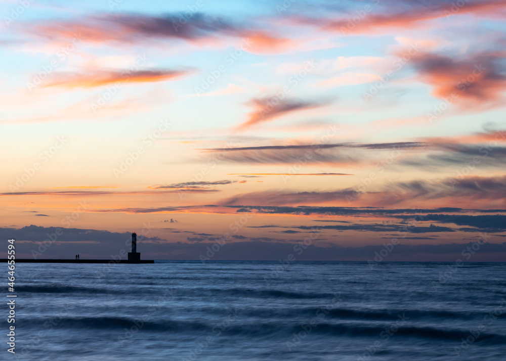 Fototapeta premium Dusk settles over the Bayfront Lighthouse in silhouette, surrounded by Lake Michigan waves,, at the Bay Overlook, in Sunset Park, Petoskey, Michigan.