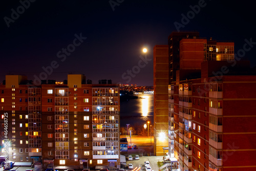 Full moon over the city. The big moon is reflected in the river. Night urban landscape.