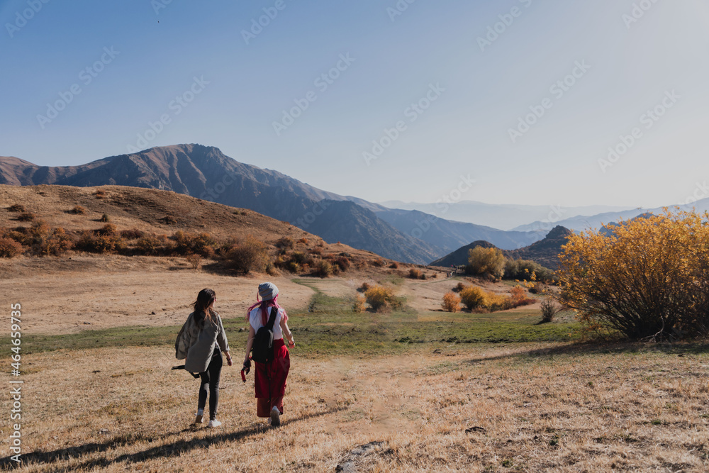 two women tourists are walking along the road among the hills and mountains