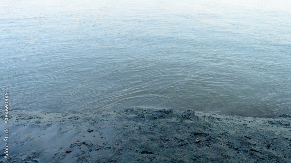 Muddy river banks in low tide next to wave water. Alluvial soils deposited by the river. Nature background. Close up.