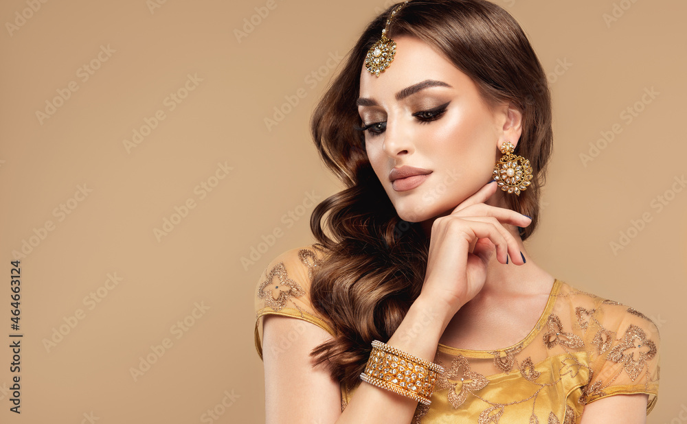 Fotka „Portrait of beautiful indian girl. Young hindu woman model with  golden kundan jewelry set, earrings, tikka and bracelet . Traditional India  costume lehenga choli or saree . Curly hair“ ze služby