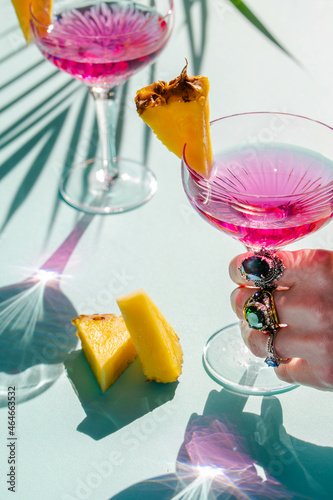A women hand with jewelry holding a cocktail glasses with campari decorated with pineapple pieces.