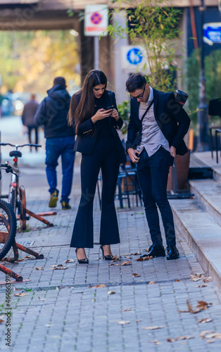 Business man and woman holding mobile phone and talking standing on the streets