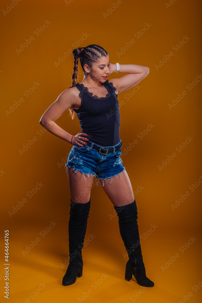 Full-length picture of a pretty urban model posing with her arm at the hip isolated on an orange background Full-length picture of a pretty urban model posing with her arm at the hip isolated on an orange background
