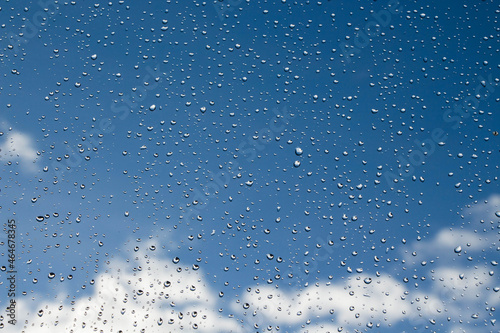 Raindrops on glass on a background of blue sky with clouds